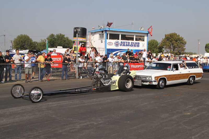 Historic, classic Top Fuel Dragsters are push-started down the return road in front of the cheering spectators.
