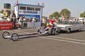 Historic, classic Top Fuel Dragsters are push-started down the return road in front of the cheering spectators.