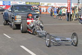 Historic, classic Top Fuel Dragsters are push-started down the return road in front of the cheering spectators.