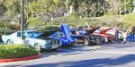 A Cobra and 5 early Ford Mustangs gather in a corner of one of the many parking lots.